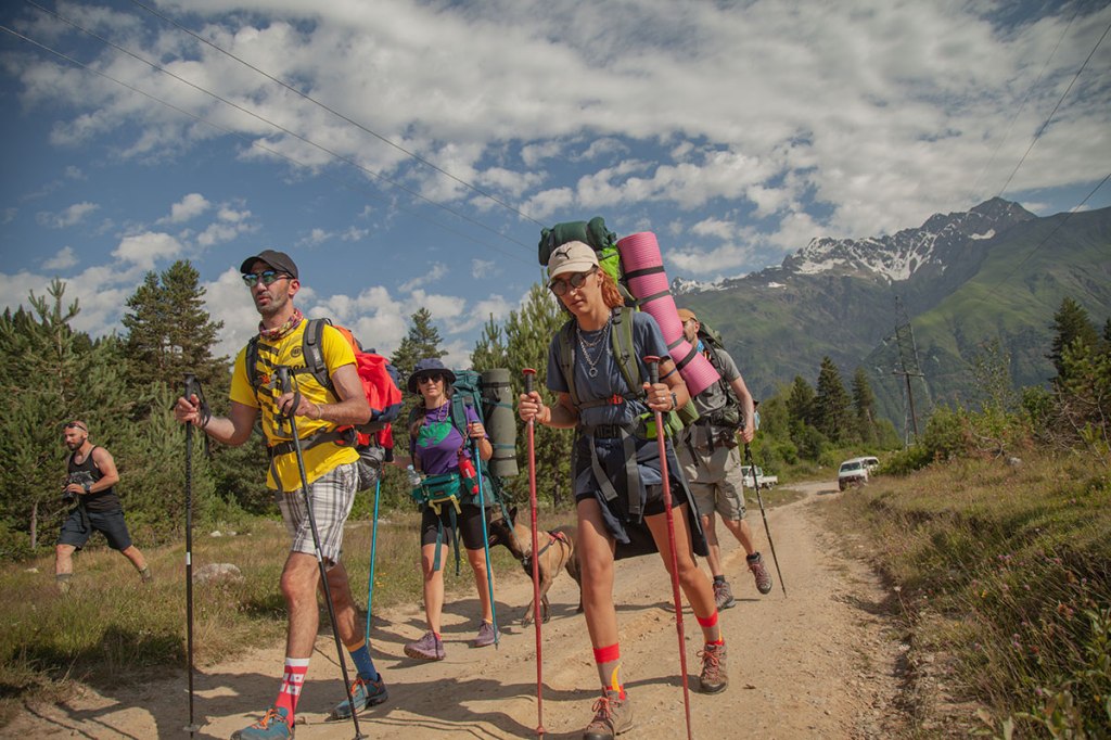 Four hikers with backpacks and dog hiking. Highlander Adventure, Biliki App
